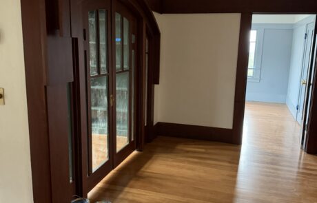 Expert Wood Staining Services for Interior Trim and Doors Dark stained wood trim around an arched doorway with glass panels in a home interior, showing detailed wood finishing.