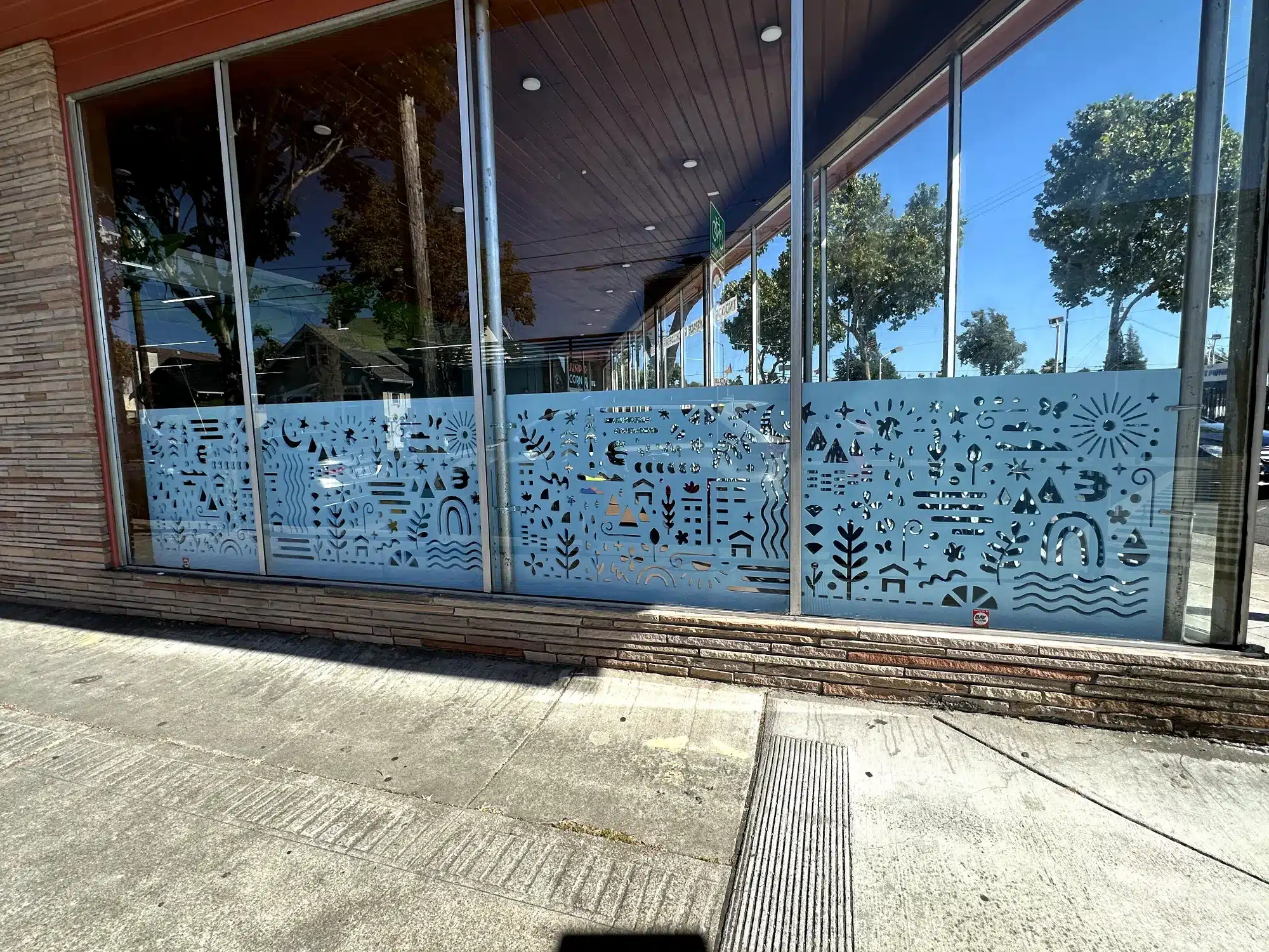 Light Blue Decorative Window Film Light blue decorative window film with geometric patterns and icons on commercial storefront glass in Oakland, CA